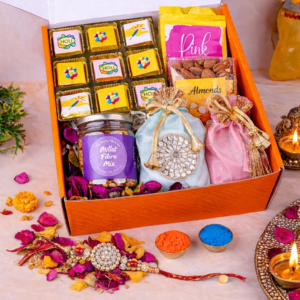 Luxury Raksha Bandhan gift hamper with designer rakhi, chocolates, dry fruits, sweets, and festive gift items arranged in an orange gift box.